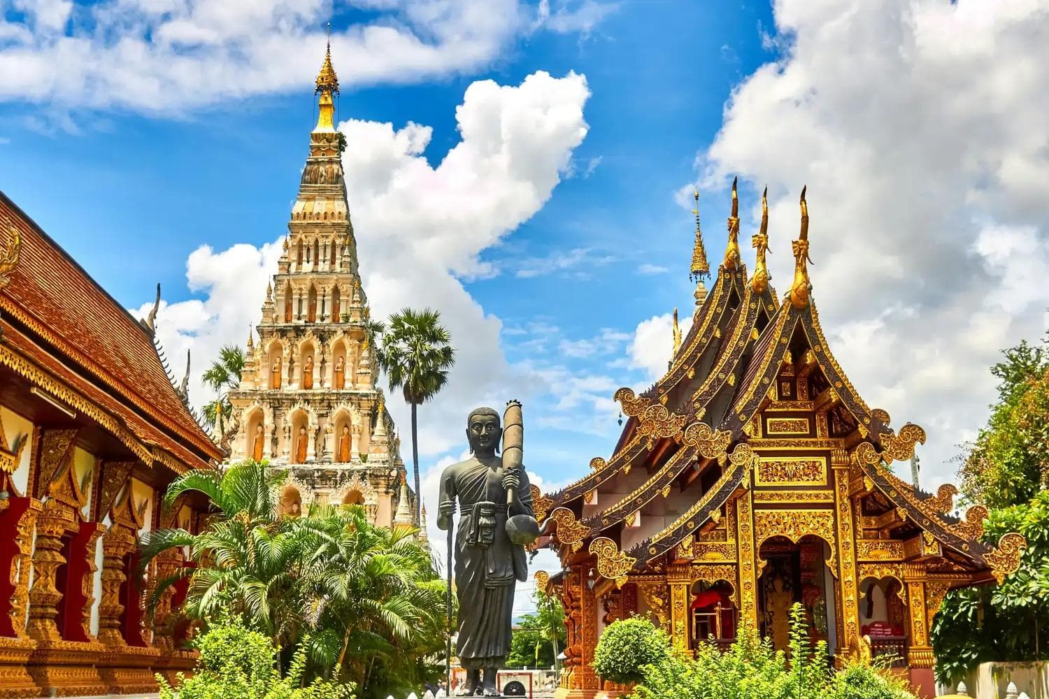 Goldverzierte Tempelgebäude, Pagode und stehende Buddha-Statue unter blauem Himmel