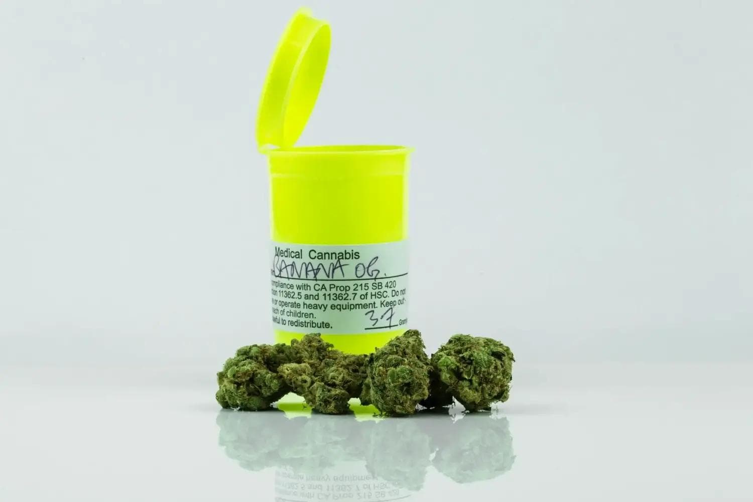 Gelbe Arzneidose mit vier Cannabisblüten auf weißem, reflektierendem Untergrund