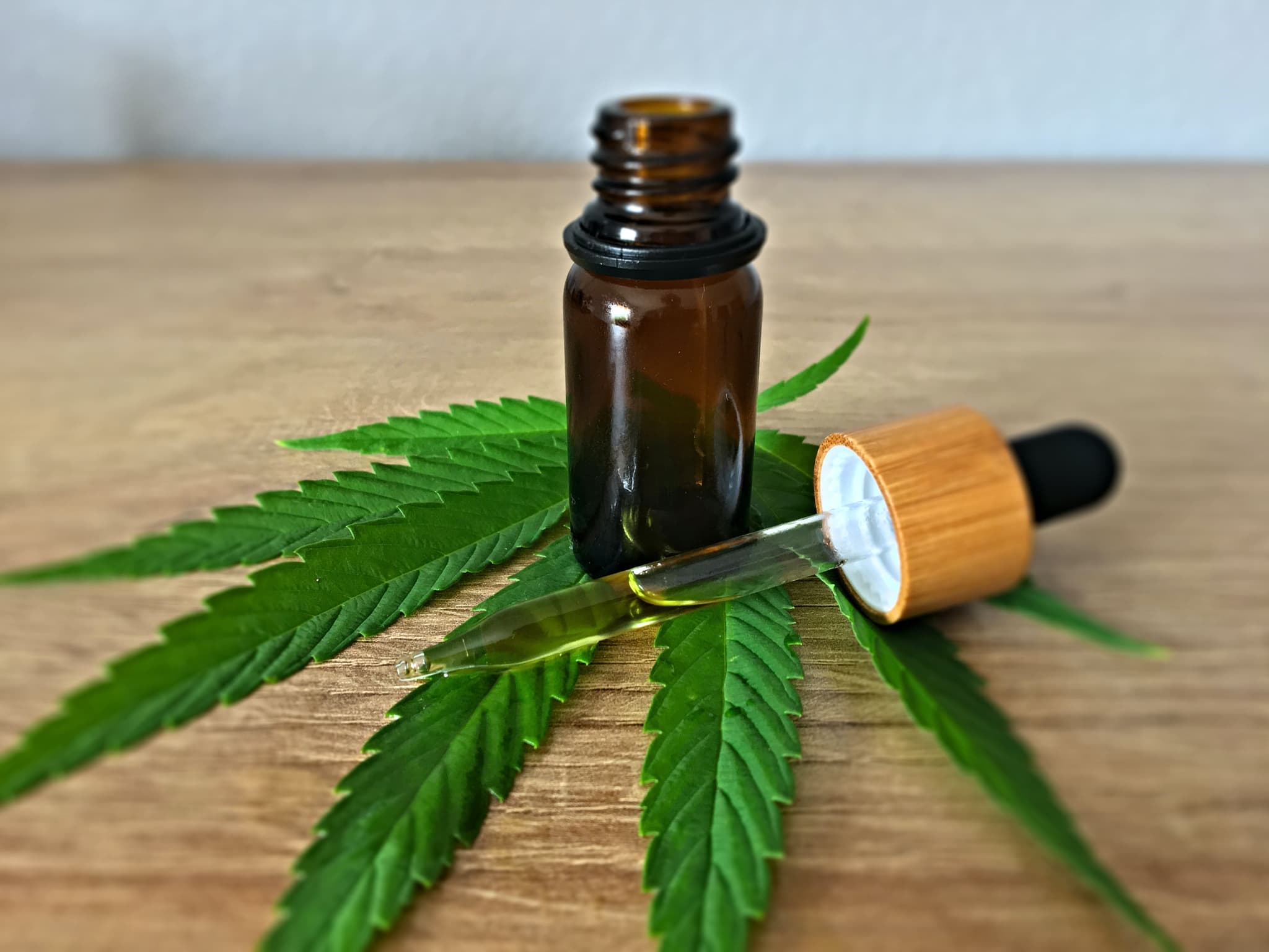 Braune Flasche und Pipette mit grünem CBD-Öl auf Hanfblättern