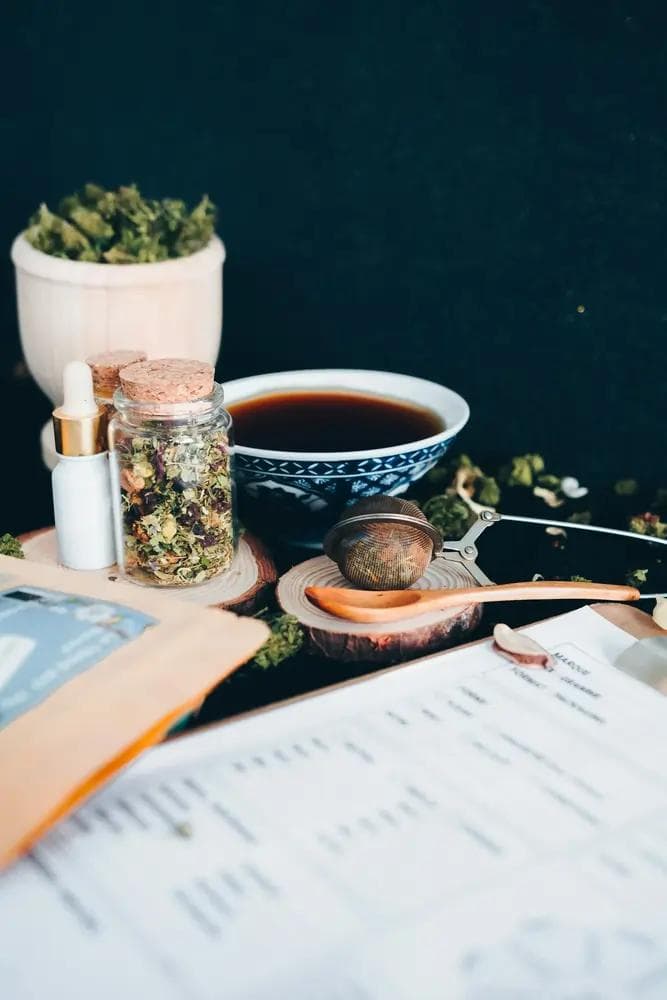 Tasse Tee, Glas mit getrockneten Blüten, Teesieb und Pipettenflasche