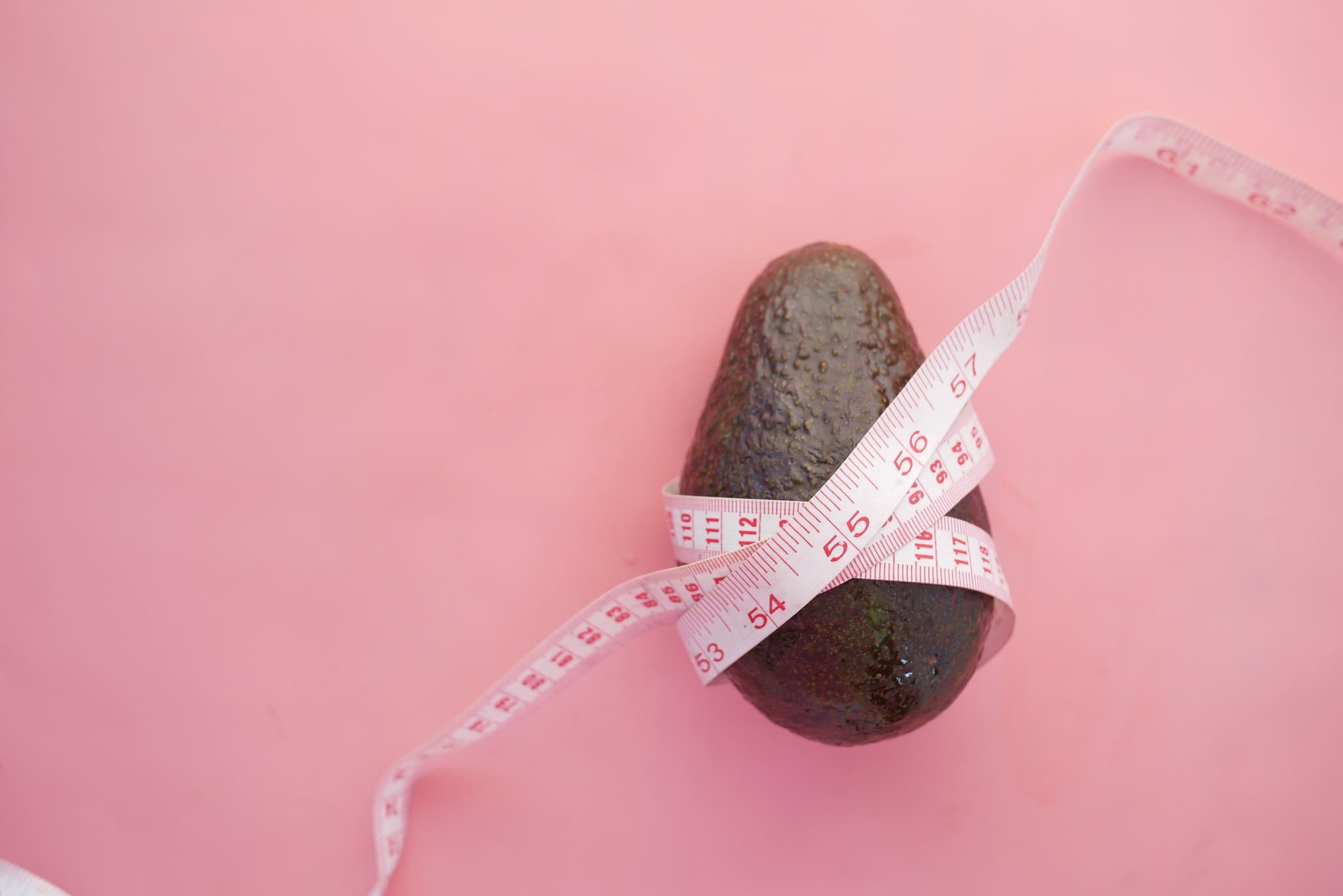 Dunkle Avocado mit weißem Maßband auf rosa Hintergrund