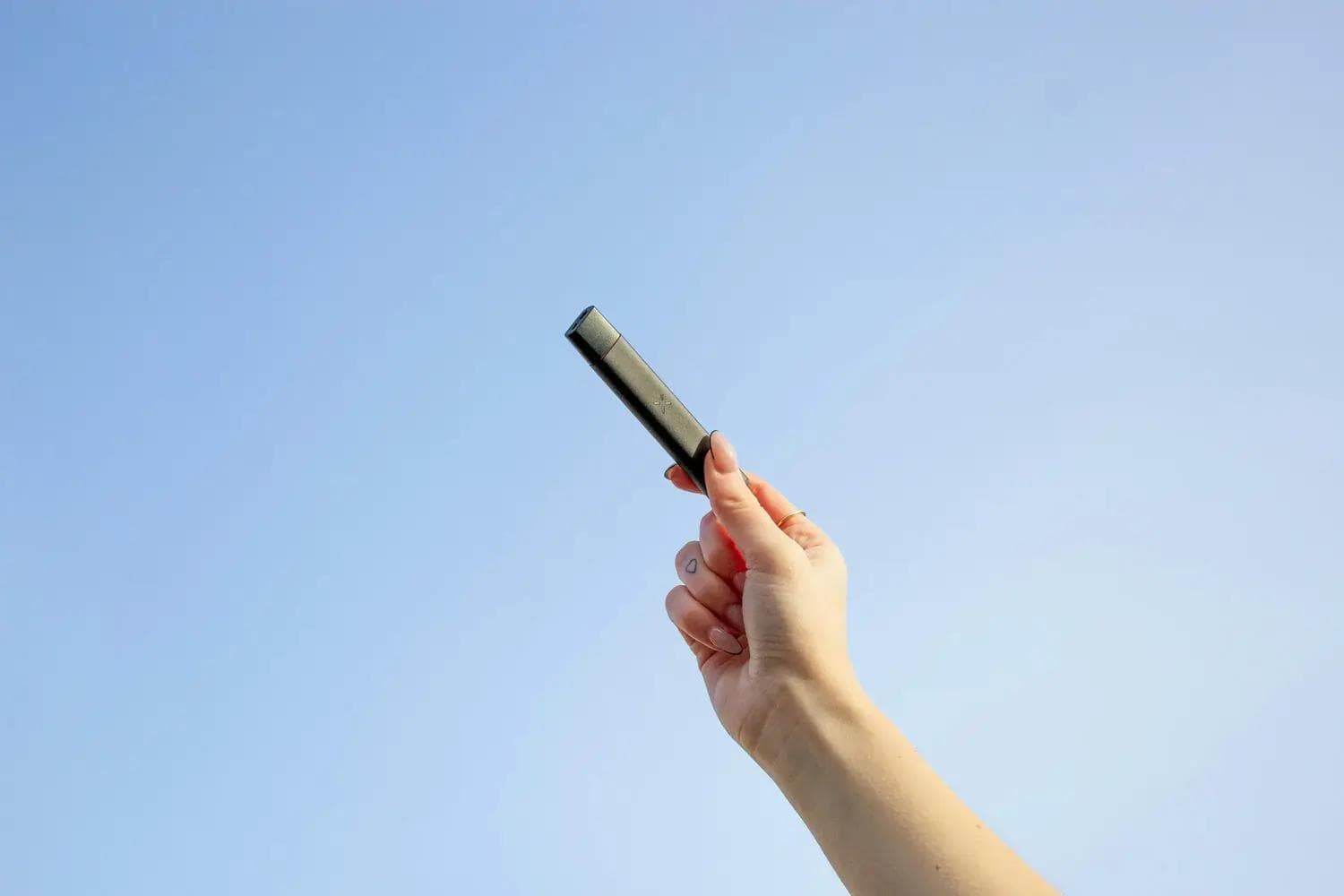 Hand hält schwarzen Vape-Pen vor blauem Himmel