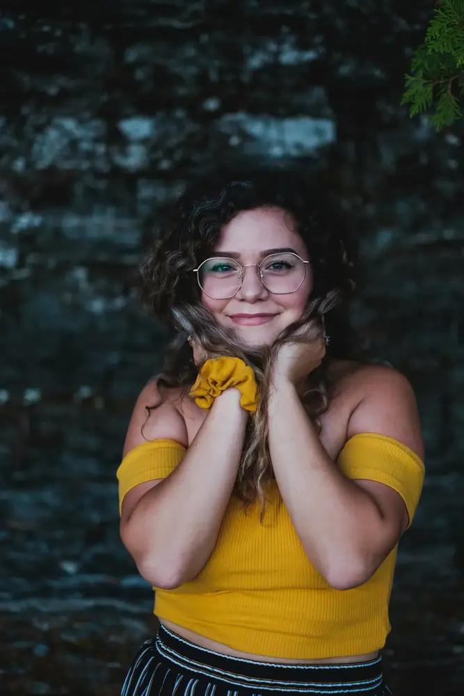 Lächelnde Frau mit Brille, lockigen Haaren und gelbem Off-Shoulder-Top