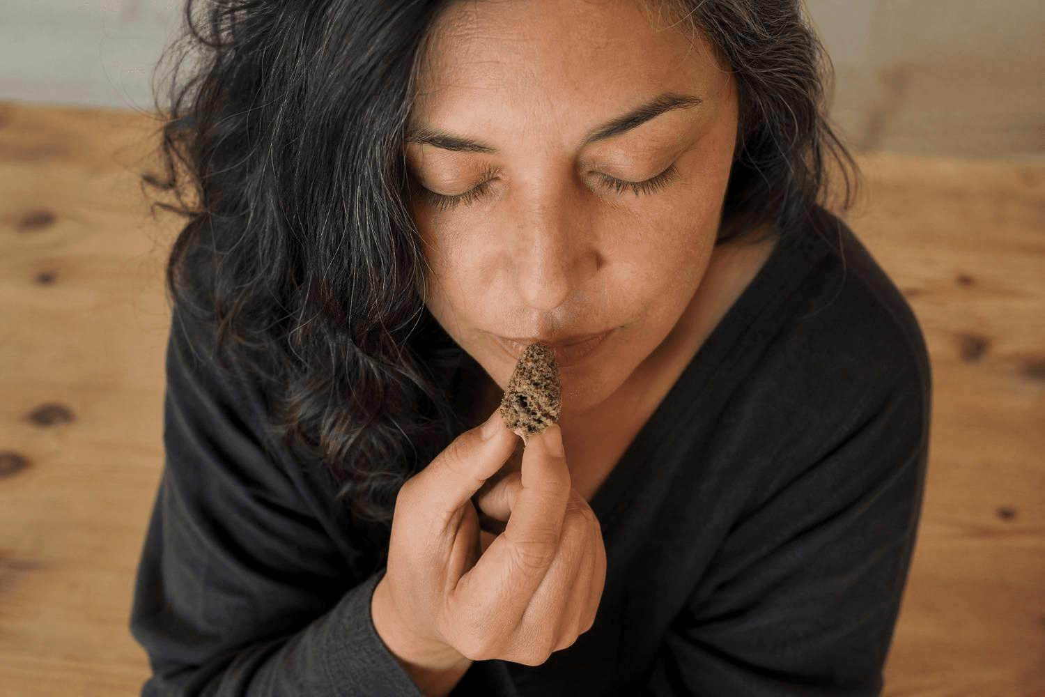 Eine Frau mittleren Alters mit geschlossenen Augen hält eine getrocknete Cannabisblüte an die Nase und riecht daran – aufgenommen leicht von oben, ruhige, konzentrierte Stimmung.